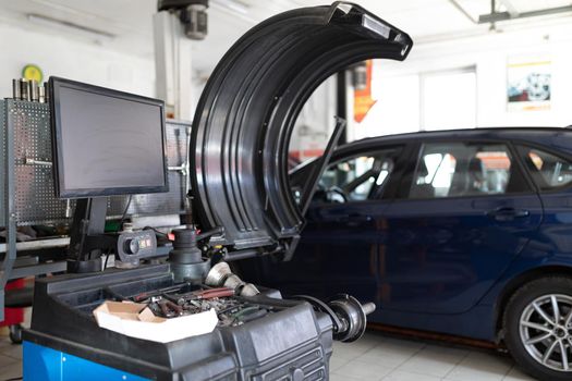 Photo of a machine for balancing wheels and repairing tires of an auto against the background of a blue passenger car at a service station