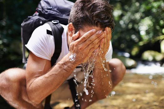 Nothing more refreshing. a young man splashing cool water on his face while hiking near a stream.