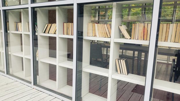 White shelving with books, behind glass, in summer