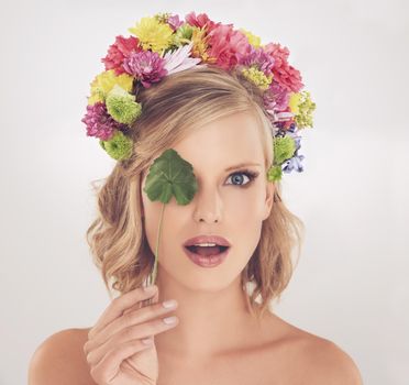See beauty in a new light. A young woman with flowers in her hair covering her one eyes with a leaf.