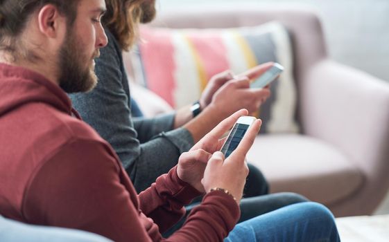 Young man using smartphone browsing social media texting messages sitting on sofa with friend