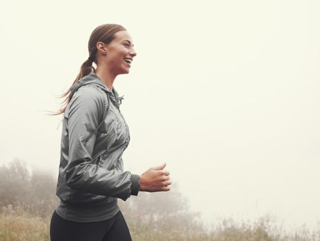 Running puts a smile on her face. A young woman jogging on a country road on a misty morning.