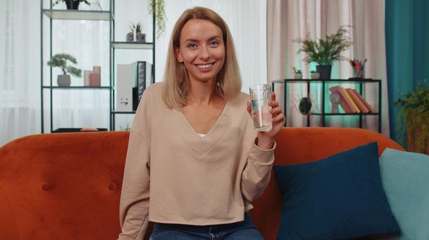 Thirsty one young woman sitting at home holding glass of natural aqua make sips drinking still water