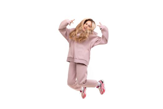 beautiful charismatic blonde in a pink tracksuit jumps on a white background, photo in a jump movement