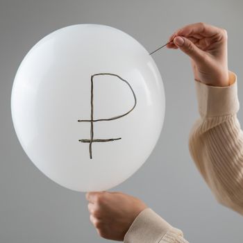 Caucasian woman pops a balloon with a ruble inscription with a needle.