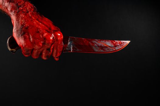 A man with bloody hands brandishes a knife on a black background.