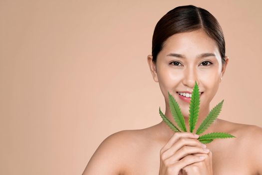 Portrait of young ardent girl with healthy fresh skin holding green hemp leaf.