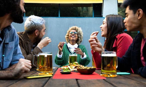 Multiracial friends enjoy some beer and laughing together in outdoors bar.