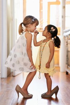 They grow up so fast...Two little girls wearing over-sized high heel shoes.