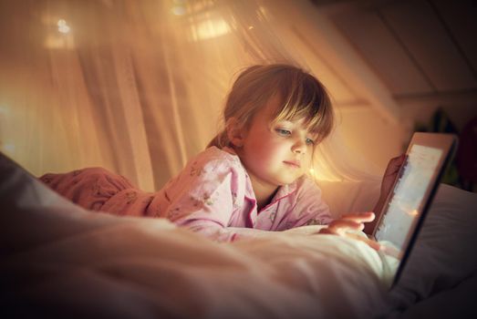 I read past my bedtime. A young girl lying on her bed while using a digital tablet.