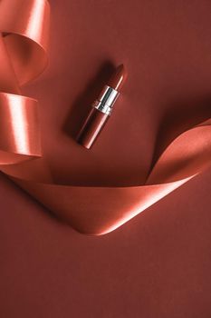 Luxury lipstick and silk ribbon on bronze holiday background, make-up and cosmetics flatlay for beauty brand product design