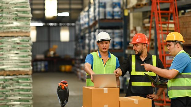 Warehouse workers and manager using laptop in a large warehouse. Manufacture storehouse occupation concept