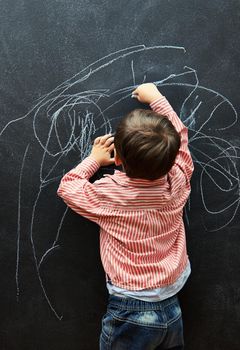 Ill call this piece Life. a little boy scribbling on a blackboard with chalk.