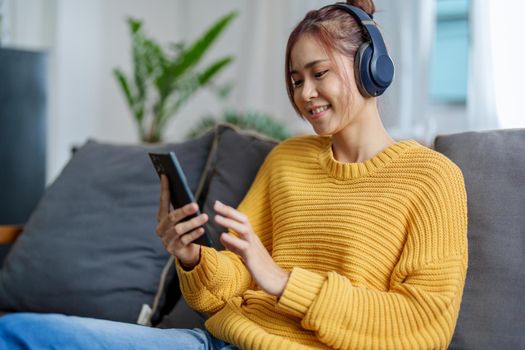portrait of a young Asian woman woman using headphones holding smartphone while sitting on sofa