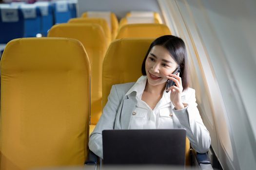 Cheerful asian businesswoman calling phone and using laptop computer during flight. Urban lifestyle