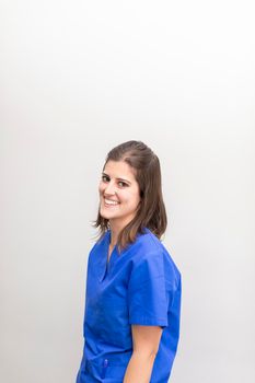 Portrait of a caucasian woman dentist, smiling with joy and looking at camera wearing blue uniform at the dental clinic