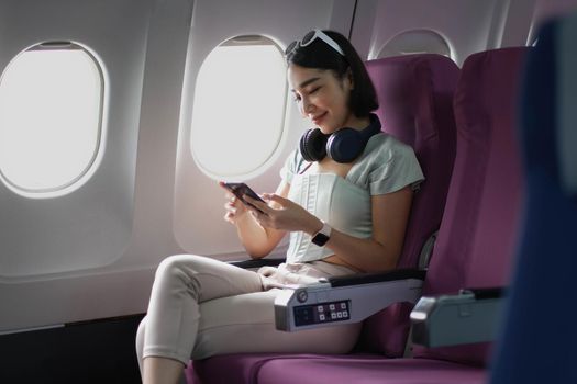 Young woman sitting with phone on the aircraft seat near the window during the flight in the airplane