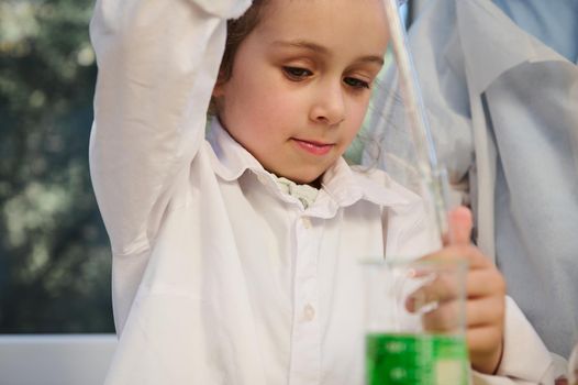 Mischievous child girl drips few drops of green chemical solution from a flask into a test tube during chemistry lesson