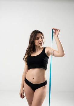 Confused brunette female with slim body in a black underwear looking on a blue measure tape. Healthy nutrition and weight losing concept. Weight loss concepts.