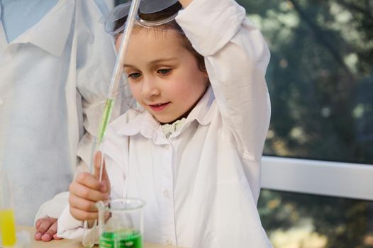 Charming smart Caucasian child girl, elementary age student conducts chemical experiment in school Chemistry laboratory