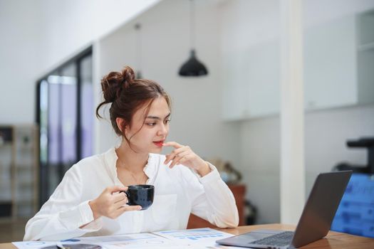 woman working on a computer, budgeting documents and drinking coffee