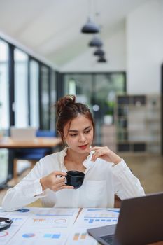 woman working on a computer, budgeting documents and drinking coffee