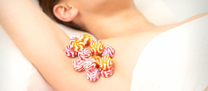 Waxing, depilation armpit concept. Colored round candies lying down on the female armpit, close up.
