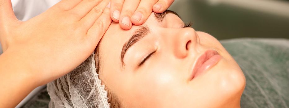 Head massage. Beautiful caucasian young white woman receiving a head and forehead massage with closed eyes in a spa salon.