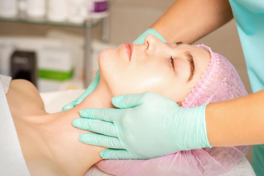 Cosmetologist with gloved hands applies a moisturizing mask with peeling cream on the female face. Facial cosmetology treatment. Procedures for facial care.