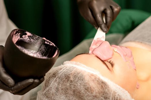 Beautiful young caucasian woman receiving an alginic mask to the face in beauty salon. Facial skin treatment.