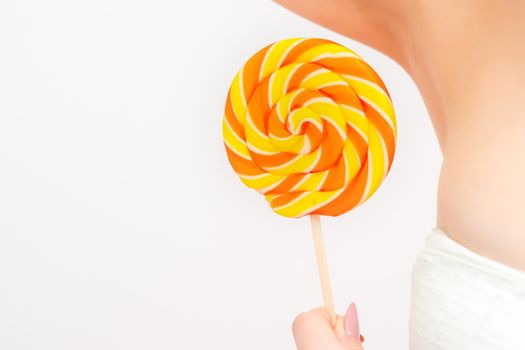 Waxing, depilation concept. A young female holds a round lollipop near her armpit on white background.