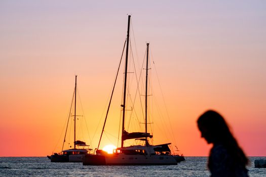 Sailboats silhouetted in the sunset with an unknown woman in the foreground