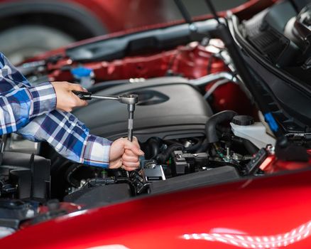 Female auto mechanic unscrewing a nut to replace a car spark plug.