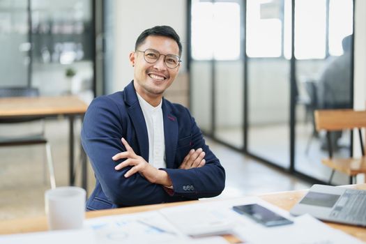 Portrait of a male business owner showing a happy smiling face as he has successfully invested his business using computers and financial budget documents at work.