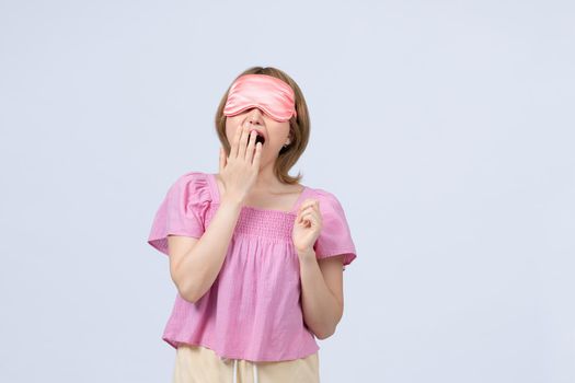 Sleepy female wakes up early, yawns, covers mouth with hand, wears sleeping mask on head, 