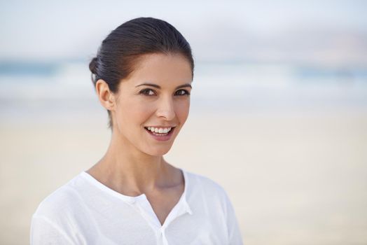 Seaside beauty. A beautiful woman standing on the beach smiling at the camera.