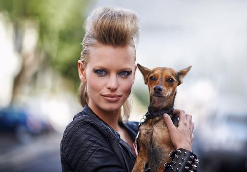 Hes the perfect pet for a rockstar. A beautiful young trendy woman holding her small dog in a city street.