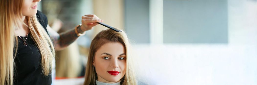 Hairdresser using comb to brush clients hair, woman on appointment in salon