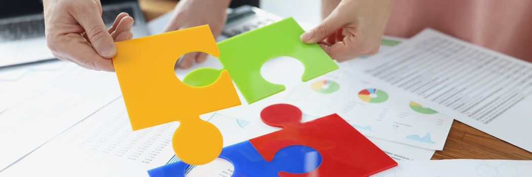 Coworkers solving jigsaw puzzle on workplace, colourful parts