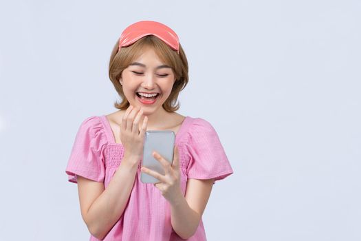 pretty asian girl with a sleep mask on her forehead chatting on smartphone  over white background