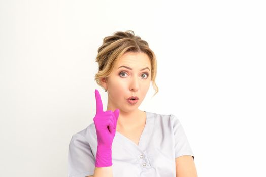 Young caucasian woman doctor wearing pink gloves keeping index finger pointed upwards making a gesture with index finger. I have an idea.