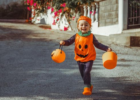 Cheerful Smiling Little Boy Dressed as Pumpkin. Taking a Lot of Sweets. Trick or Treat. Happy Halloween Tradition.