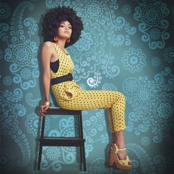 Shes one funky chic. A young woman wearing a 70s retro jumpsuit while sitting on a stool in the studio.