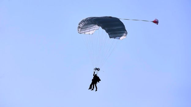 A skydiver with a white parachute canopy against a blue sky and white clouds, close-up.