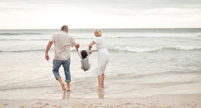 Family, children and beach with a girl and her grandparents by the sea or ocean in nature. Sand, water and summer with a senior man, woman and their granddaughter on holiday or vacation by the coast