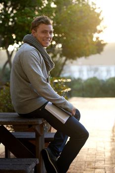 College life is the life for me. Portrait of a young man sitting on campus bench.