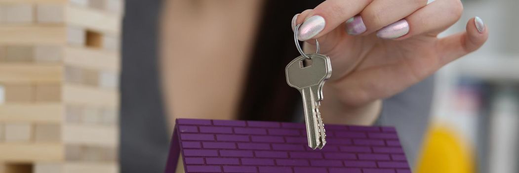 Female worker hand hold key to unlock new miniature toy house, buy new accommodation