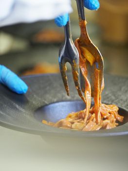closeup of a chef hand wearing gloves serving and decorating a plate of pasta