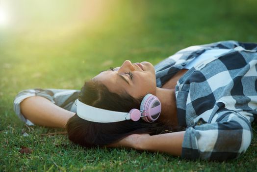 Drift away on a song...A young woman lying on her back in a park listening to music on her headphones.