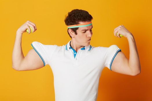 My muscles are real, I swear. A caucasian male using tennis balls as muscle for his arms while pulling a silly pose in tennis wear.